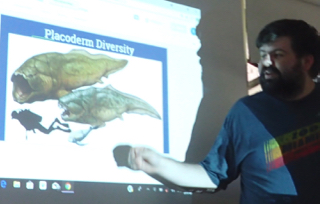 Photo of Robbie Stewart with illustration of Devonian period Placoderm fish