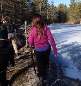 Photo of Macoun Club members walking a rocky shoreline in pine country