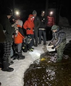 Photo of Macoun Club members crowding to the edge of the ice at night to see Mudpuppy salamanders brought out of the water alive
