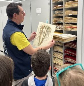 Photo of collections technician Nathan Stevens-Cocco showing Macoun Club members a plant specimen in the national herbarium